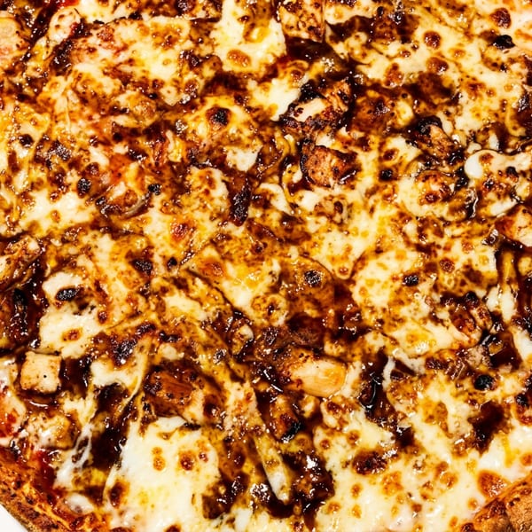 Close-up overhead view of a whole BBQ chicken pizza with melted cheese and dark sauce.